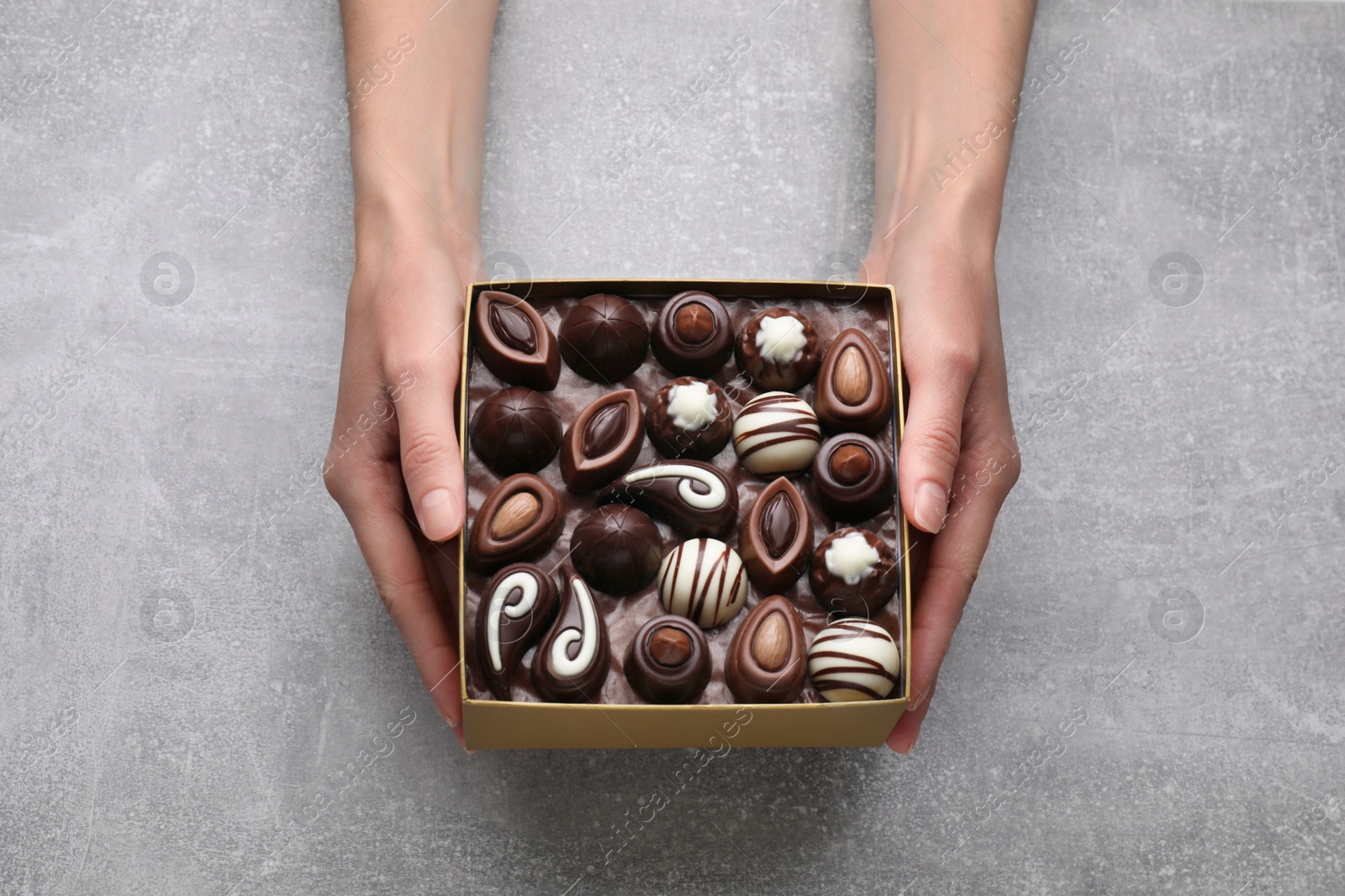 Photo of Woman with box of delicious chocolate candies at light grey table, top view