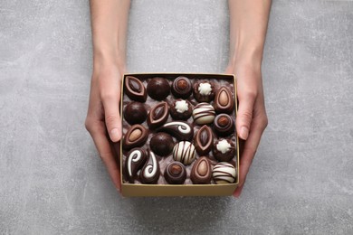 Photo of Woman with box of delicious chocolate candies at light grey table, top view