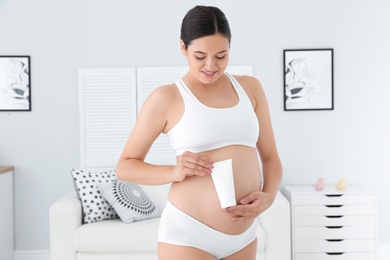 Photo of Pregnant woman holding body cream at home