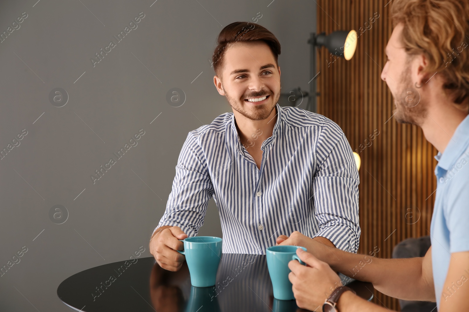 Photo of Happy gay couple with coffee at table indoors