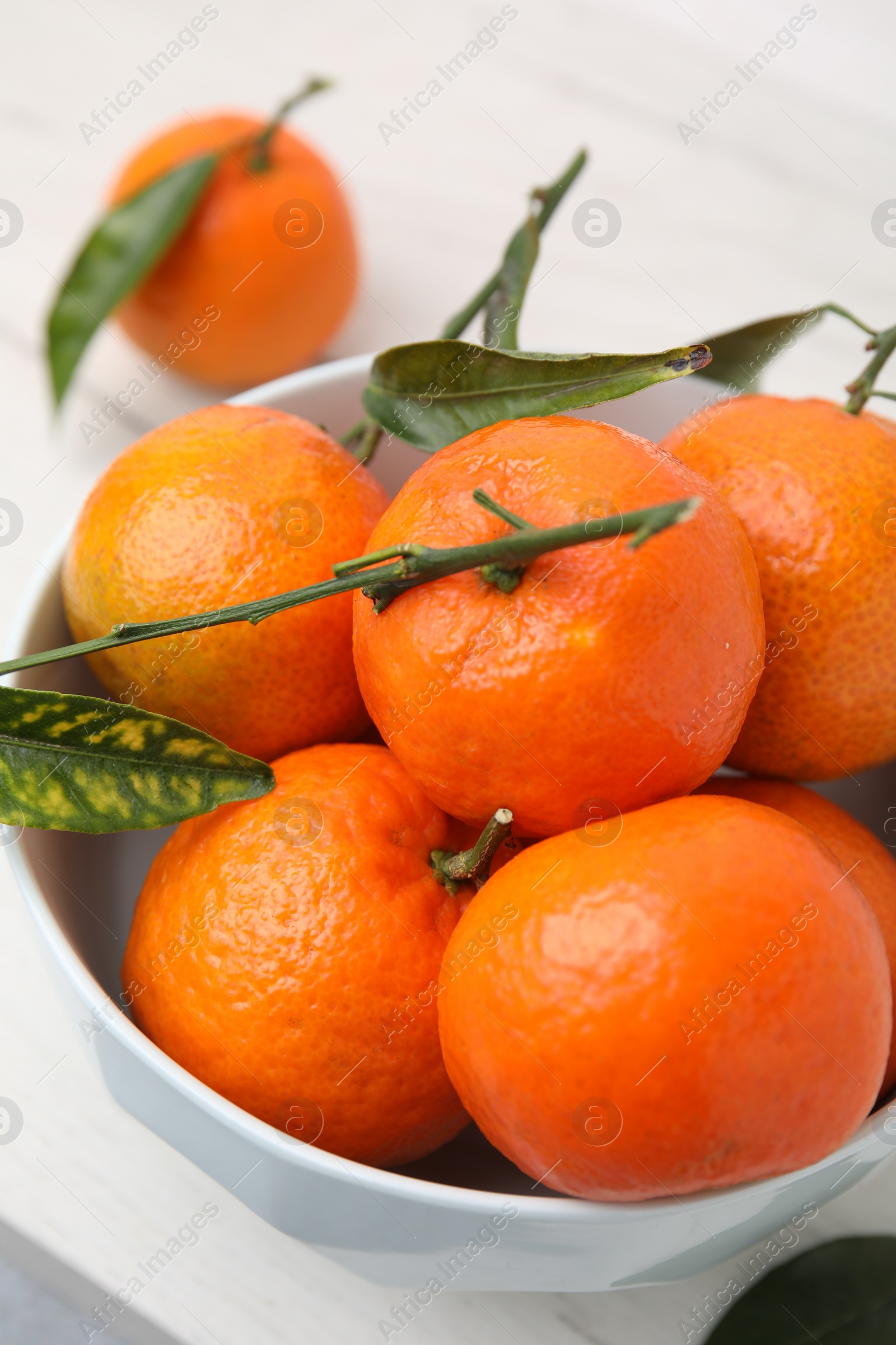 Photo of Fresh ripe tangerines and leaves in bowl on white table, closeup