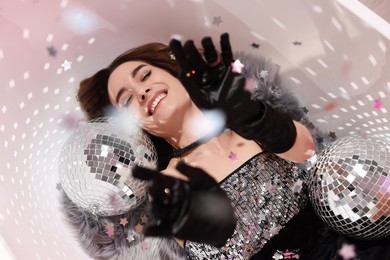 Photo of Beautiful woman in gorgeous dress among disco balls under falling confetti in bathtub, above view