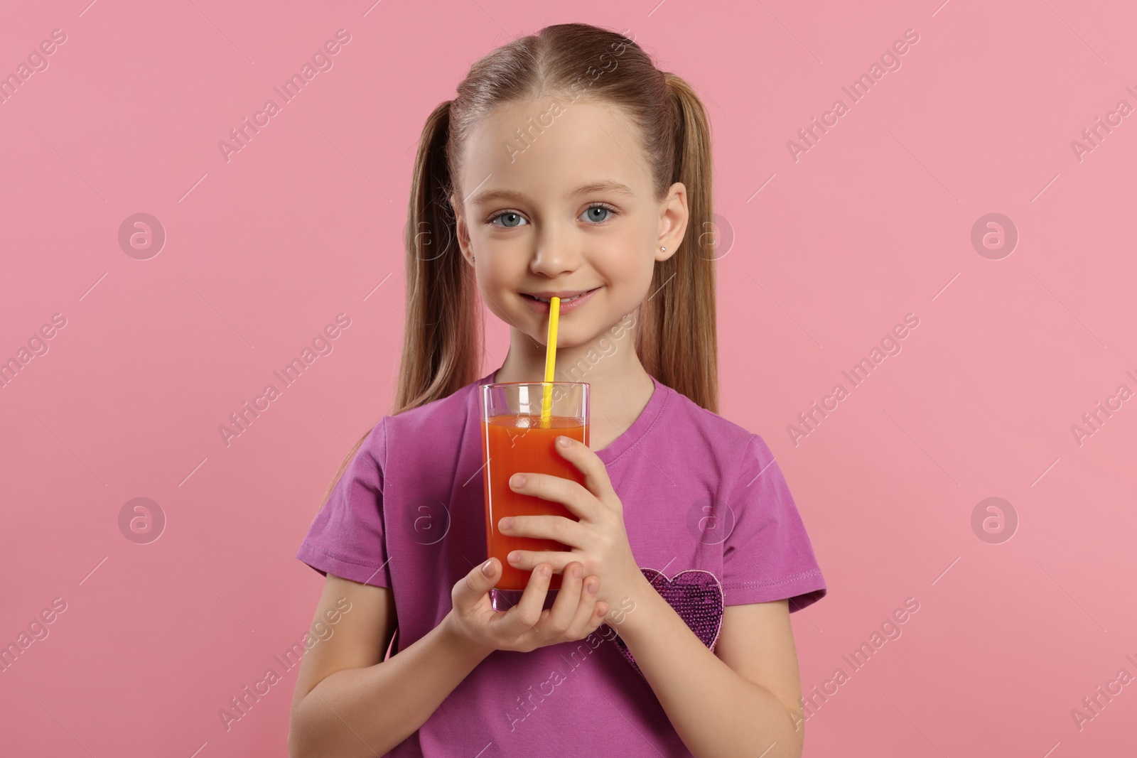 Photo of Cute little girl drinking fresh juice with straw on pink background