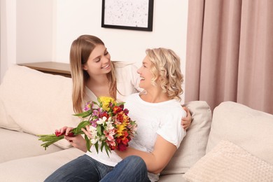 Photo of Young daughter congratulating her mom with flowers at home. Happy Mother's Day