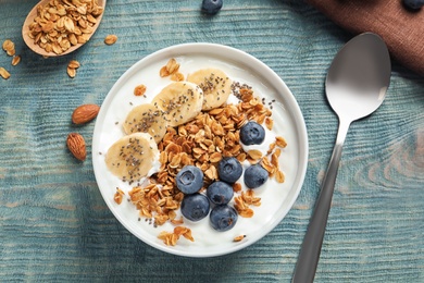Photo of Bowl of yogurt with blueberries, banana and oatmeal on color wooden table, flat lay