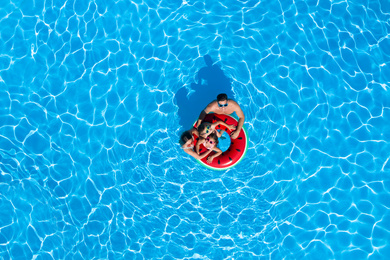 Image of Happy family with inflatable ring in swimming pool, top view. Summer vacation