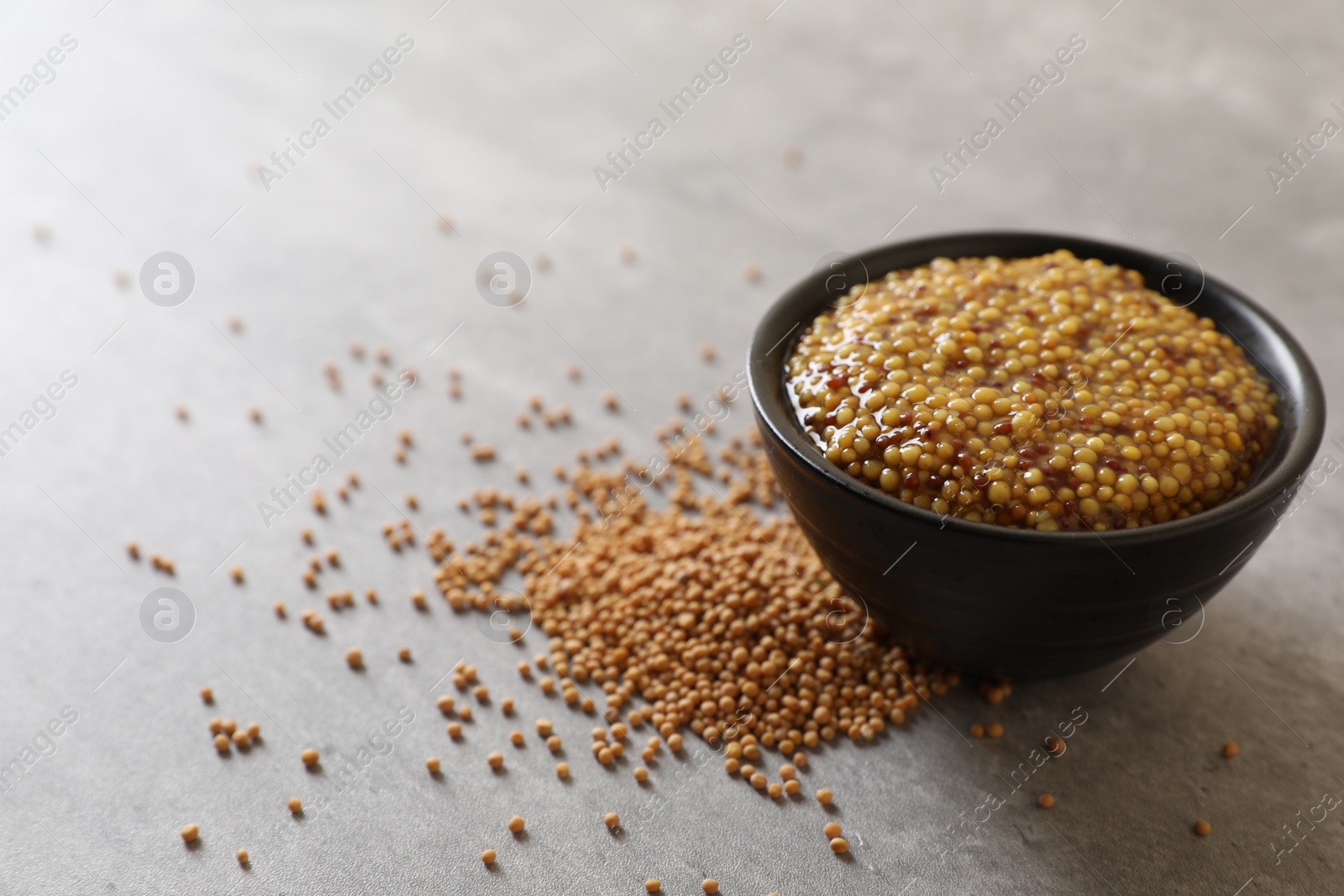 Photo of Bowl of whole grain mustard and seeds on grey table