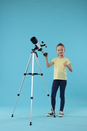 Photo of Happy little girl with telescope showing thumb up on light blue background