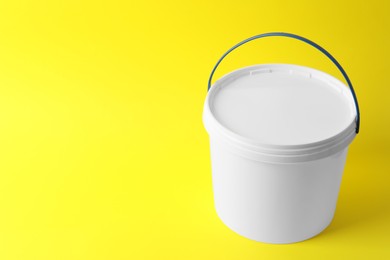 Photo of One plastic bucket with lid on yellow background. Space for text