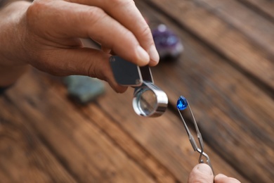 Male jeweler evaluating precious gemstone at table in workshop, closeup