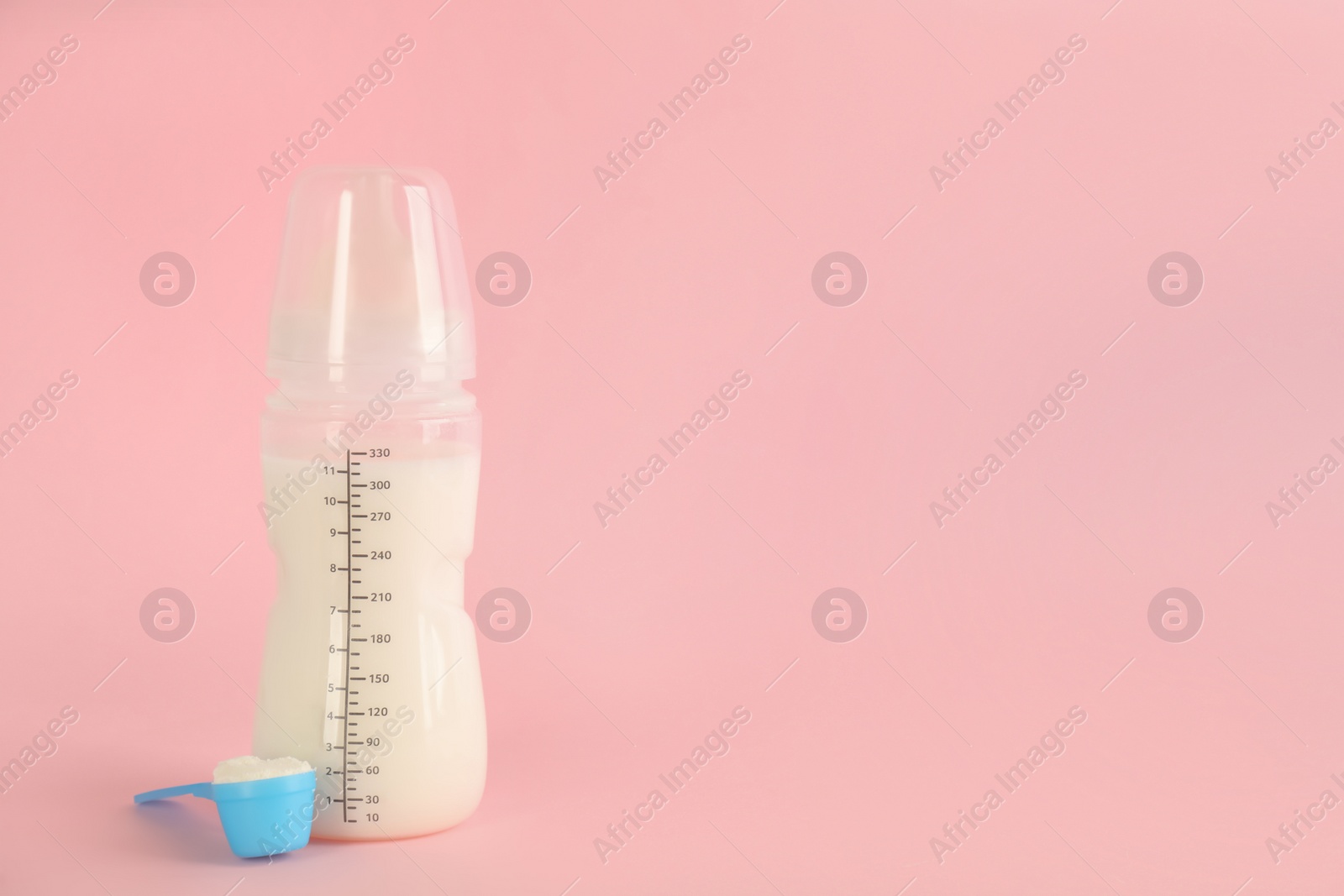 Photo of Feeding bottle with infant formula and scoop of powder on pink background, space for text. Baby milk