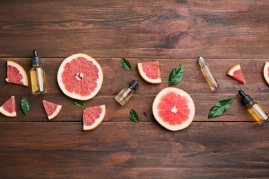 Flat lay composition with grapefruit slices and bottles of essential oil on wooden background