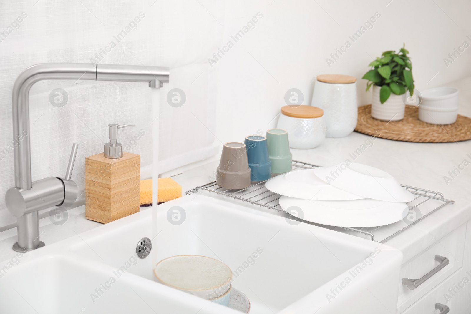 Photo of Drying rack with clean dishes near sink in stylish kitchen