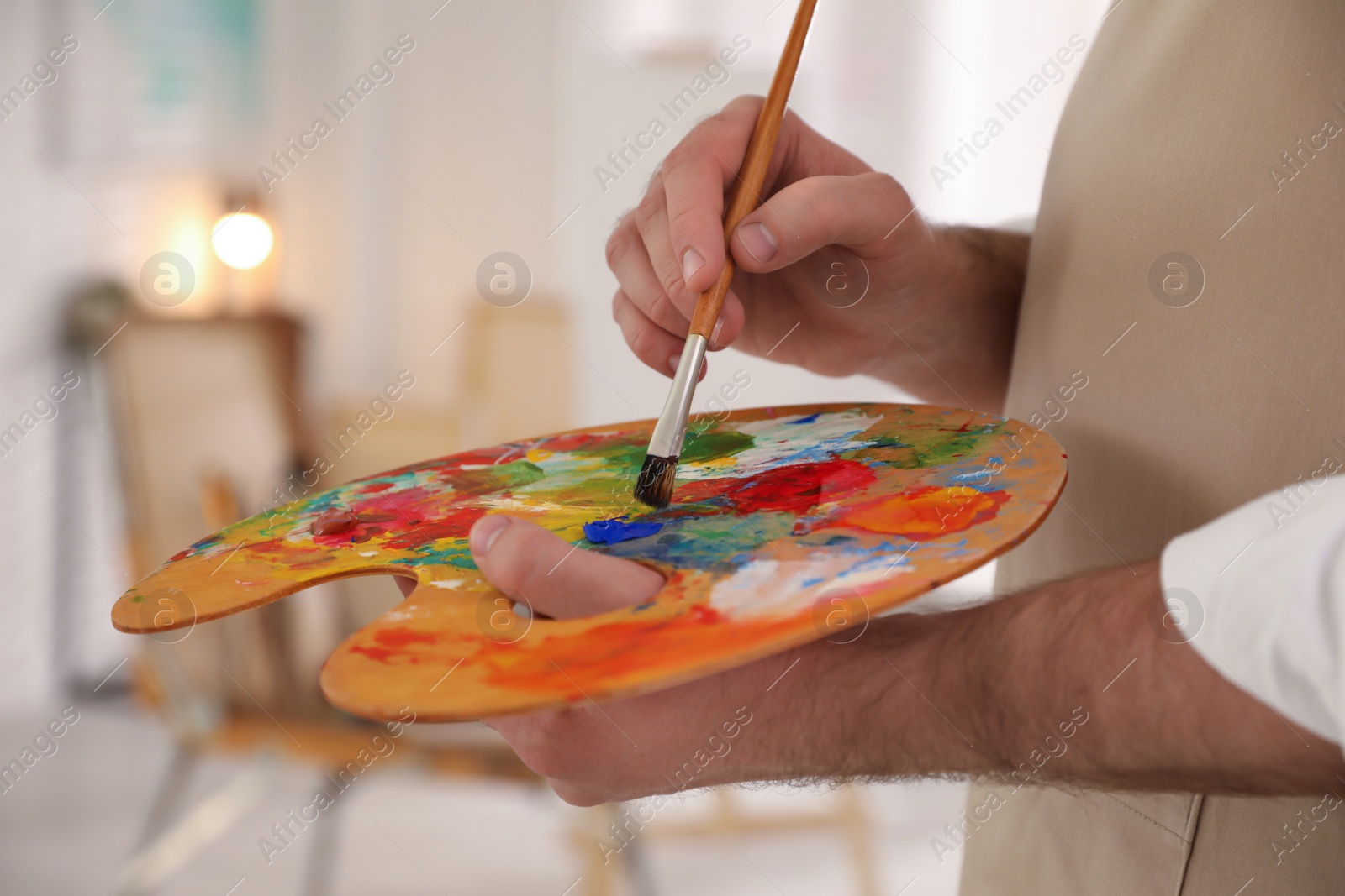 Photo of Young man with painting brush and palette in artist studio, closeup