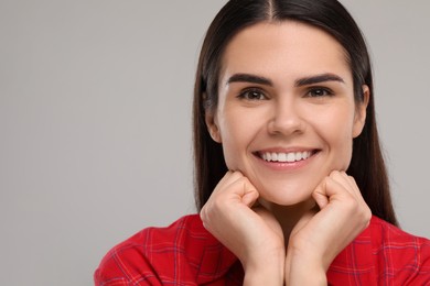 Young woman with clean teeth smiling on light grey background. Space for text