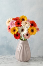 Photo of Bouquet of beautiful colorful gerbera flowers in vase on white marble table against light blue background