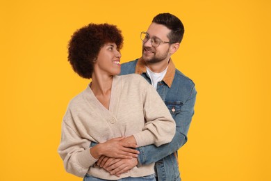 Photo of International dating. Happy couple hugging on orange background,