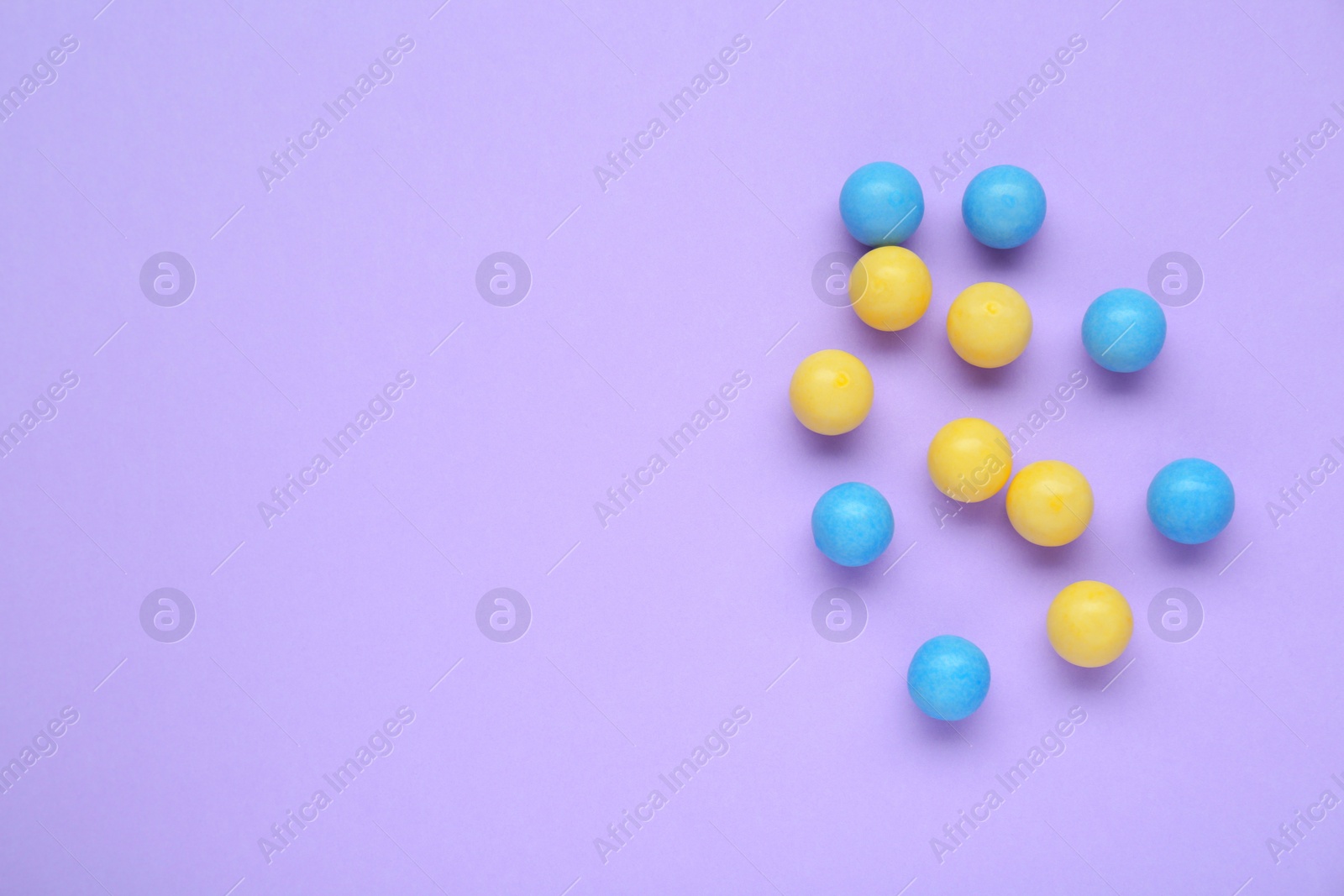 Photo of Many bright chewy gumballs on lilac background, flat lay. Space for text