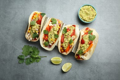 Photo of Delicious tacos with guacamole, meat and vegetables served on grey table, flat lay