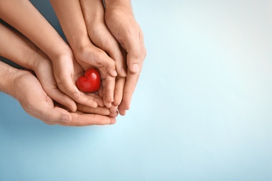 Photo of Family holding small red heart in hands on color background