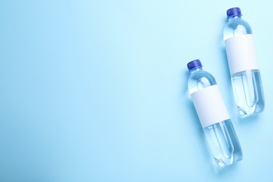 Plastic bottles of water with blank labels on light blue background, flat lay. Space for text