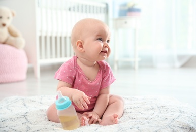 Photo of Pretty baby with bottle sitting on floor in room