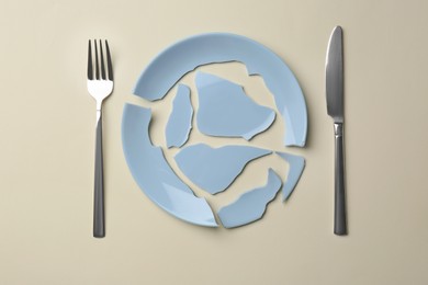 Pieces of broken ceramic plate and cutlery on beige background, flat lay