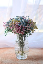 Beautiful gypsophila flowers in vase on textured table near window