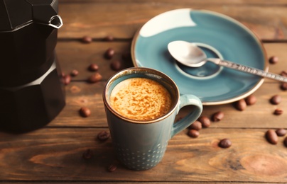 Cup of aromatic hot coffee and beans on wooden table