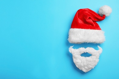 Santa Claus hat and beard on light blue background, flat lay. Space for text