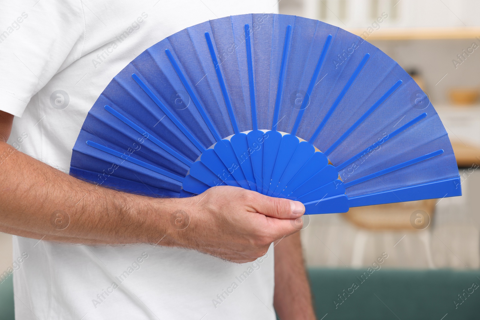 Photo of Man with blue hand fan in kitchen, closeup