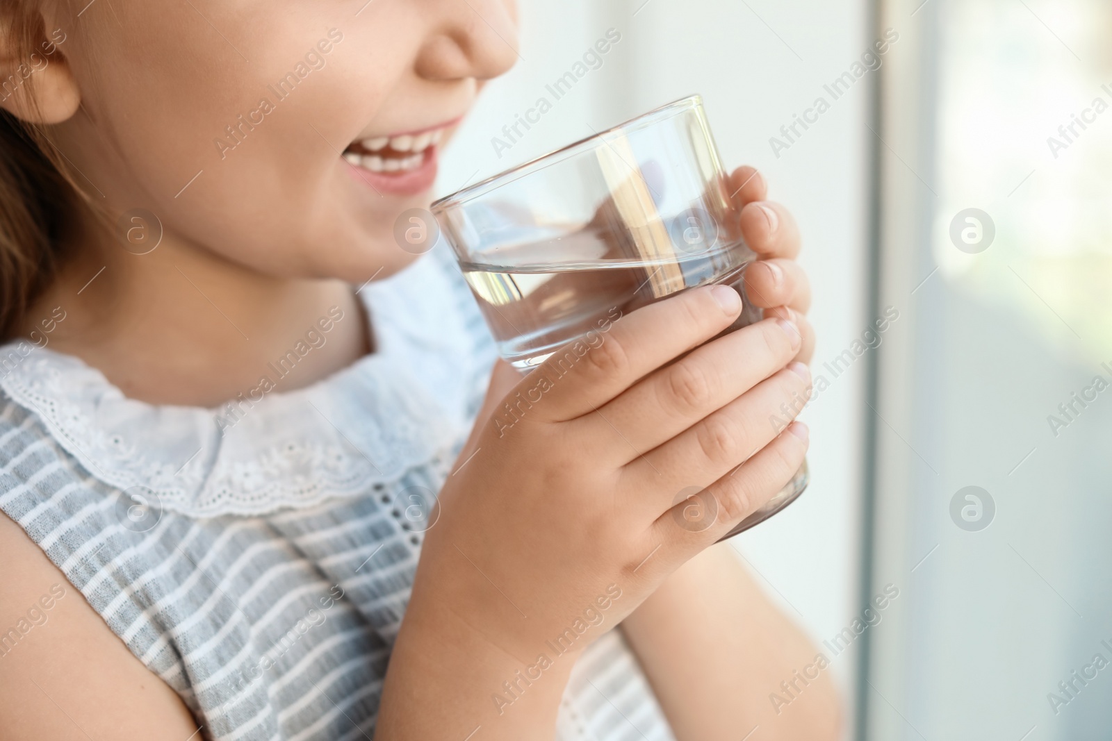 Photo of Cute little girl holding glass of fresh water at home, closeup