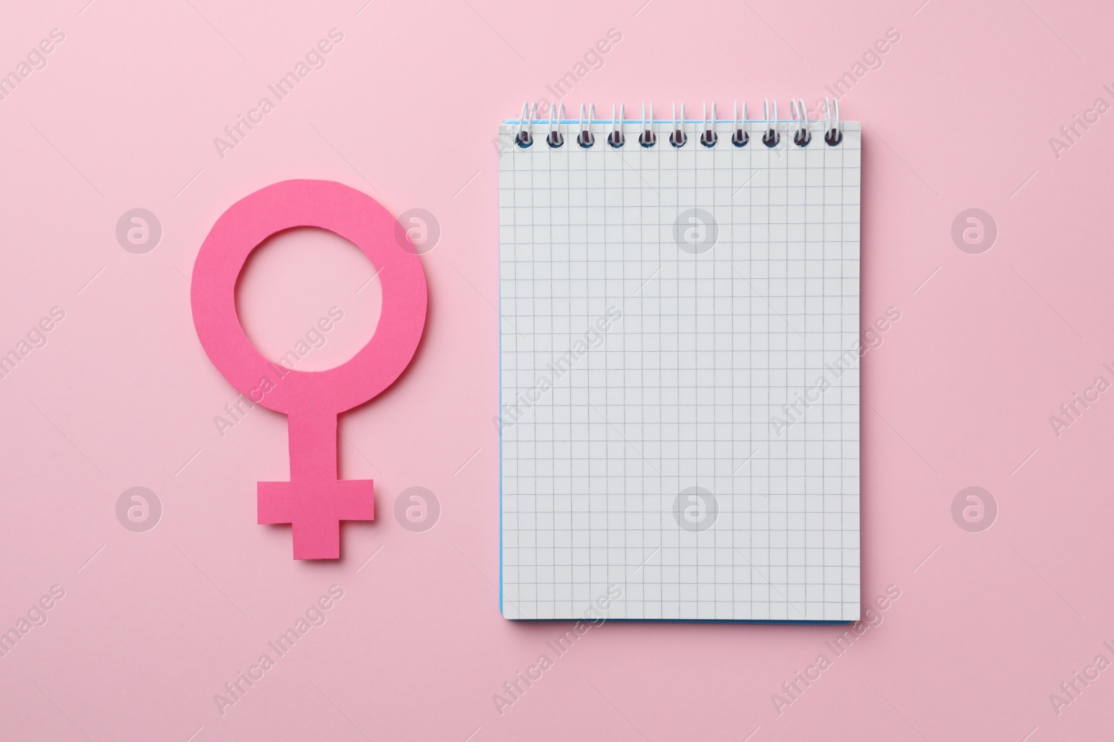 Photo of Female gender sign as women's health symbol and notebook on pink background, flat lay. Space for text