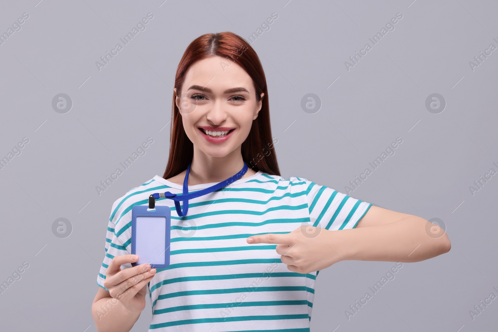 Photo of Smiling woman pointing at vip pass badge on light grey background
