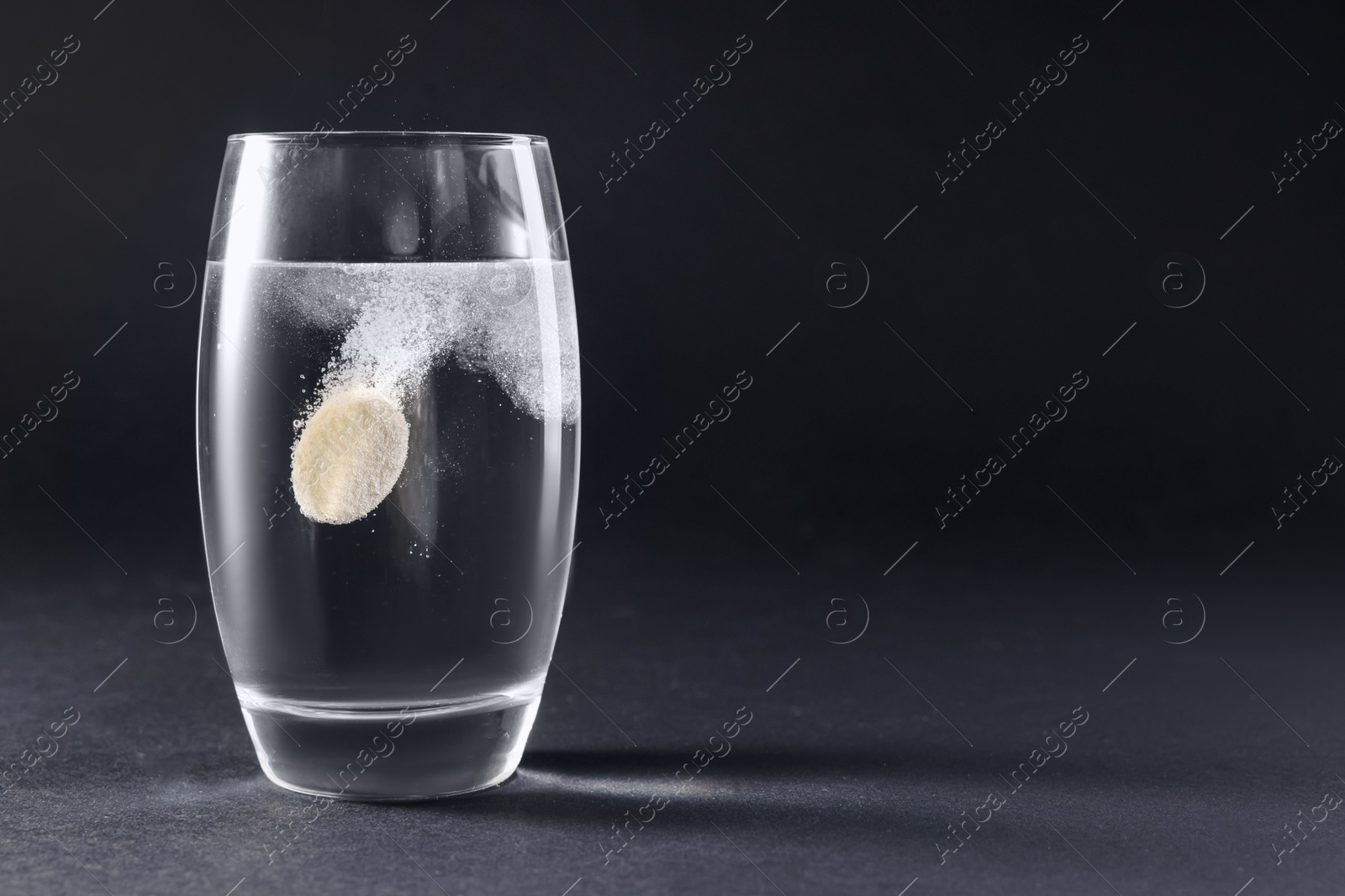 Photo of Effervescent pill dissolving in glass of water on grey table. Space for text