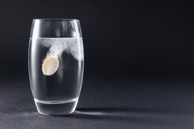 Effervescent pill dissolving in glass of water on grey table. Space for text