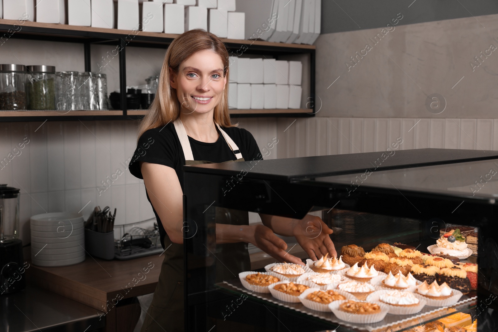 Photo of Happy seller taking delicious dessert from showcase in bakery shop