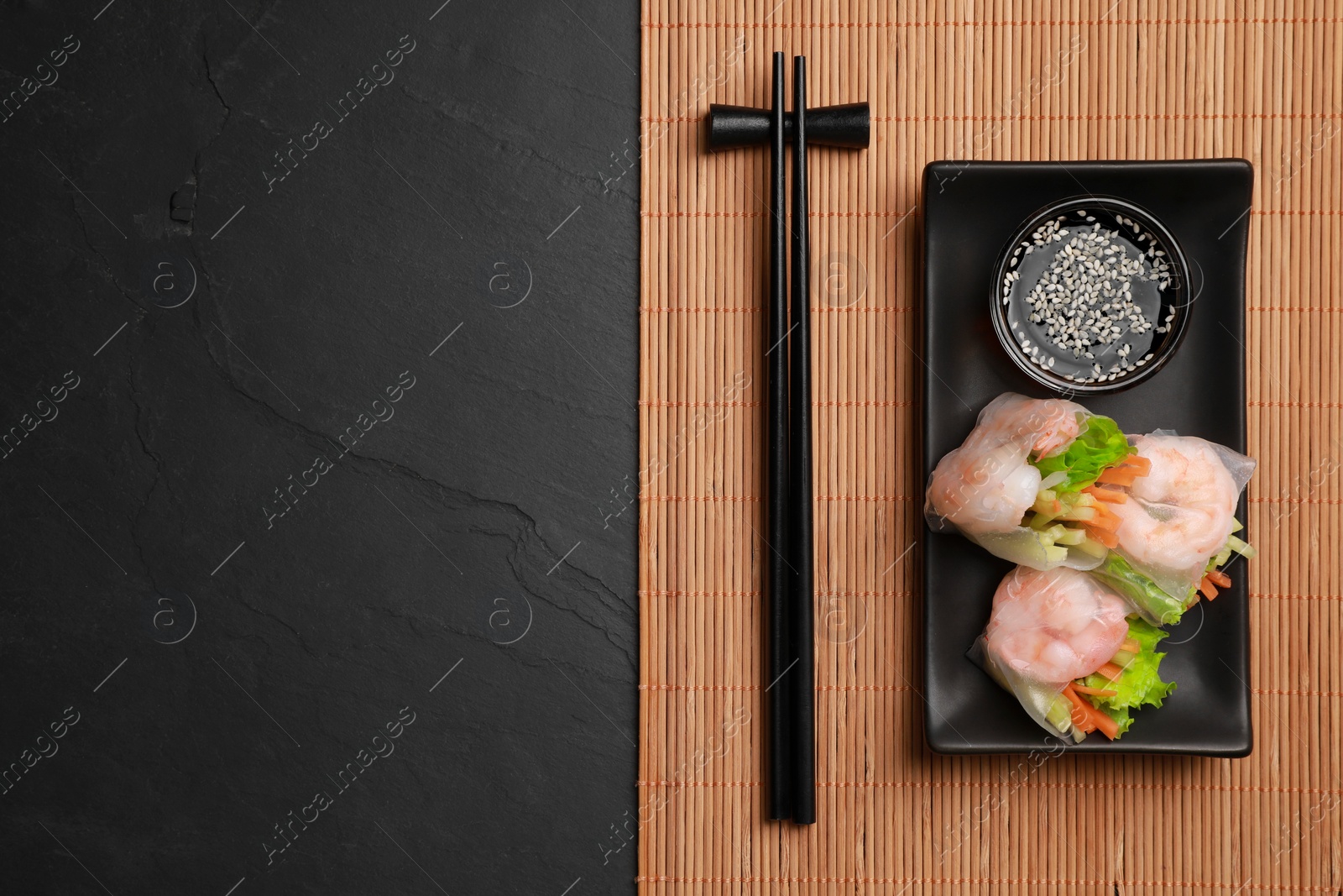 Photo of Tasty spring rolls served with soy sauce on dark grey textured table, top view. Space for text