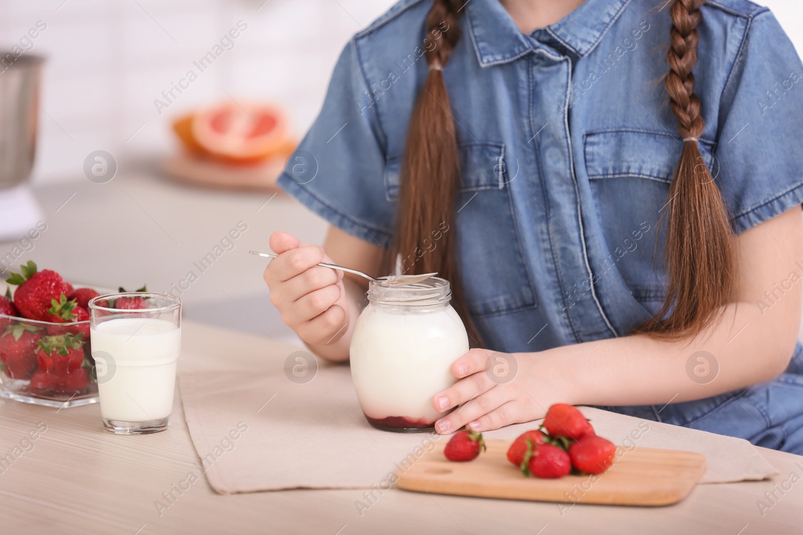 Photo of Cute girl eating tasty yogurt at table, closeup