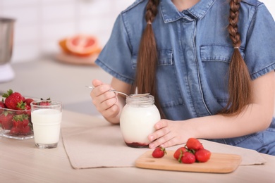 Cute girl eating tasty yogurt at table, closeup