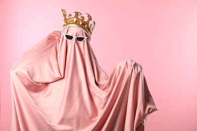 Glamorous ghost. Woman in sheet with sunglasses and crown on pink background, space for text