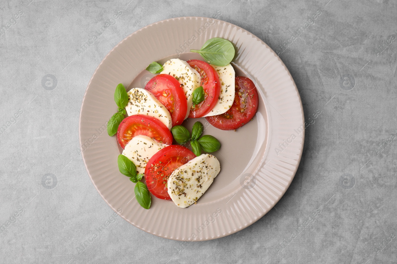 Photo of Delicious Caprese salad with tomatoes, mozzarella, basil and spices on light grey table, top view