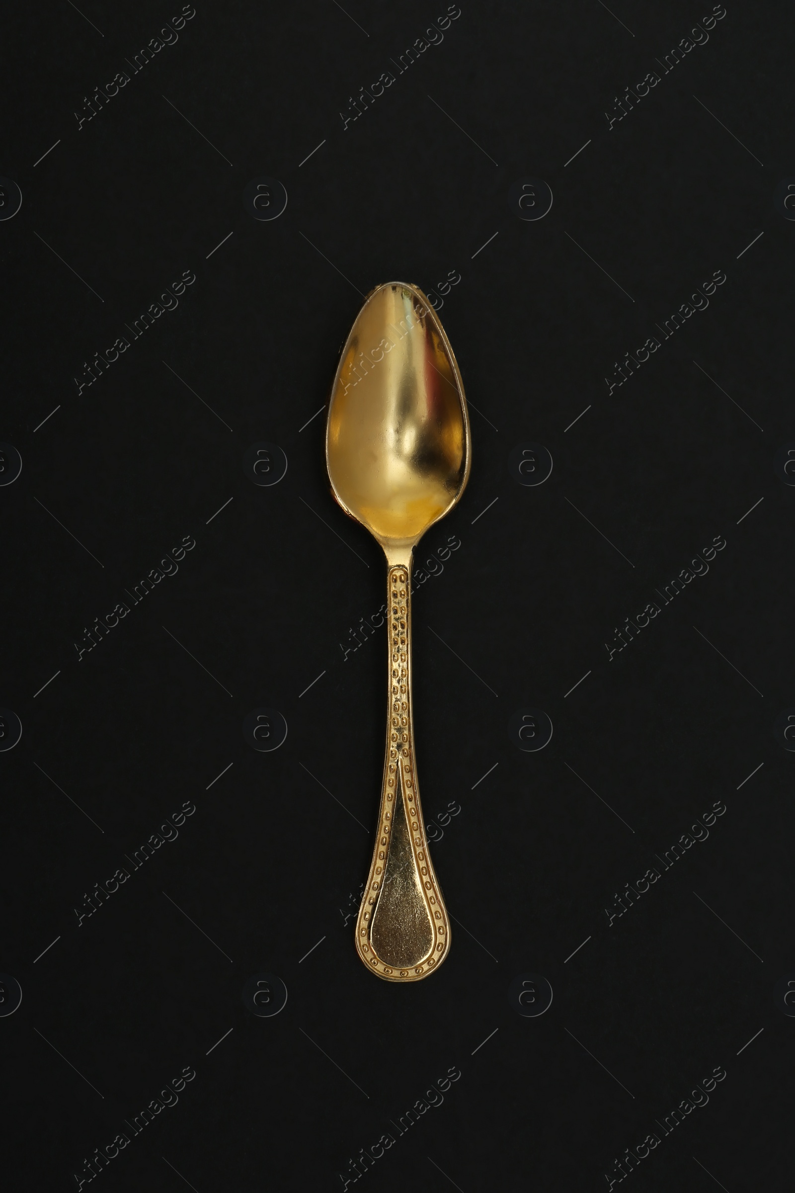Photo of Shiny gold spoon on black background, top view