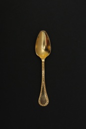 Shiny gold spoon on black background, top view