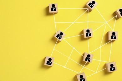 Teamwork. Wooden cubes with human icons linked together symbolizing cooperation on yellow background, top view. Space for text