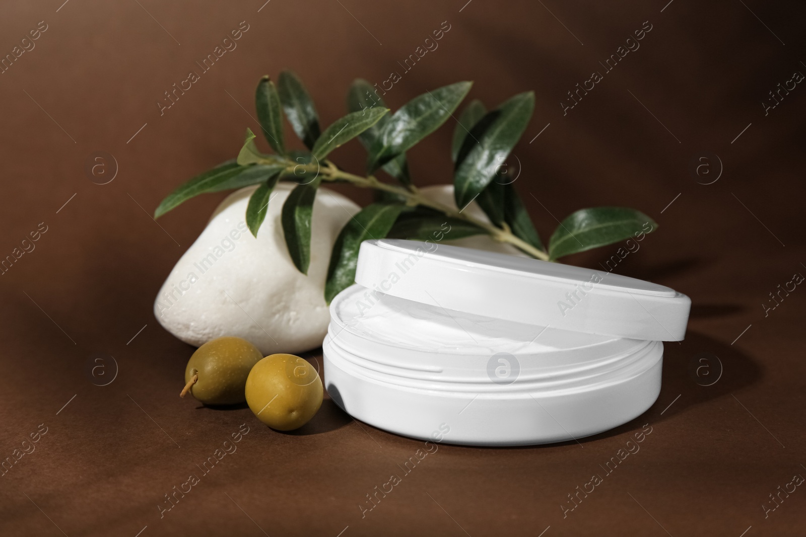 Photo of Jar of natural cream, stone and olives on brown background. Cosmetic products