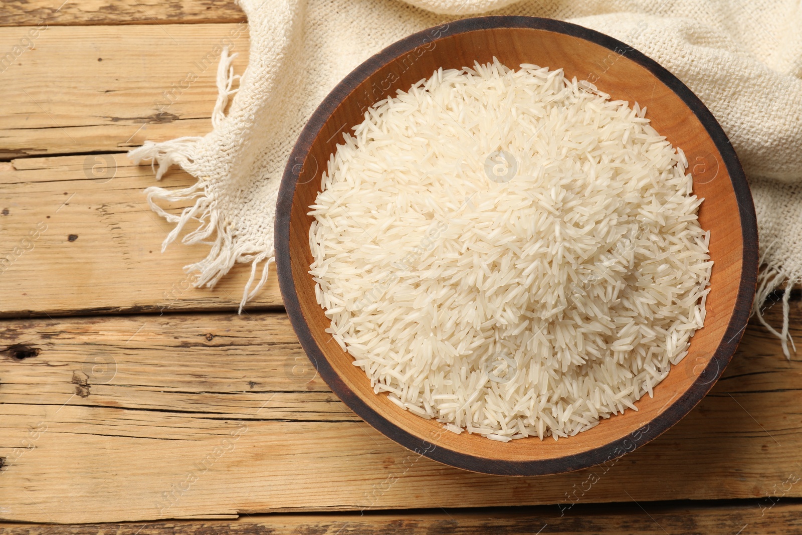 Photo of Raw basmati rice in bowl on wooden table, top view. Space for text