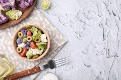 Delicious salad with cauliflower, tomato and olives served on white textured table, flat lay. Space for text