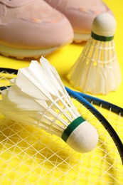 Photo of Feather badminton shuttlecocks, rackets and sneakers on yellow background, closeup