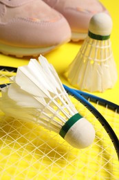 Feather badminton shuttlecocks, rackets and sneakers on yellow background, closeup